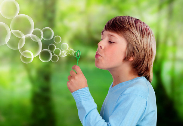 Очаровательный мальчик-подросток, дующий в поисках пузырьков в парке
 - Фото, изображение
