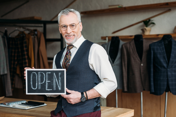handsome mature tailor holding chalkboard with open sign at sewing workshop - Photo, Image