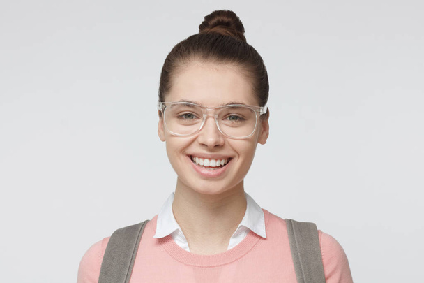 Headshot picture of young European Caucasian lady isolated on grey background dressed in casual pink pullover and wearing plastic transparent glasses showing friendliness and optimism with smile - Valokuva, kuva