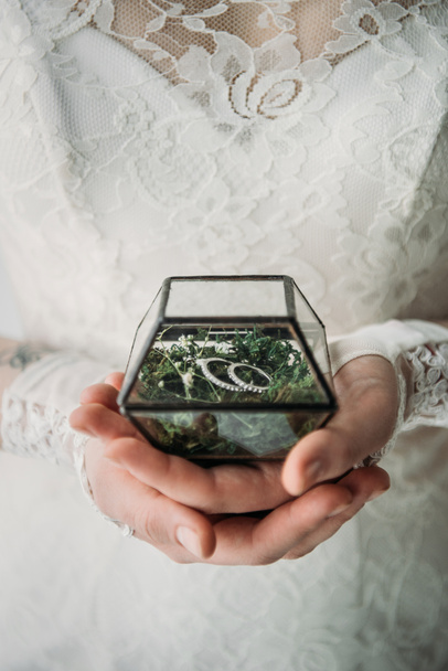 обрізаний знімок нареченої в білій сукні з обручками в коробці в руках
 - Фото, зображення