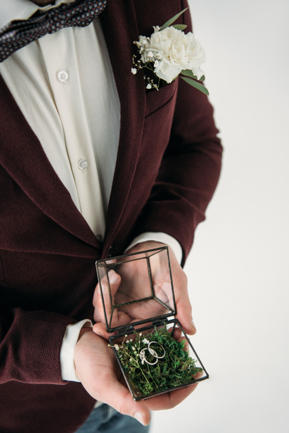 partial view of groom in suit with buttonhole and wedding rings in box in hands - Foto, immagini