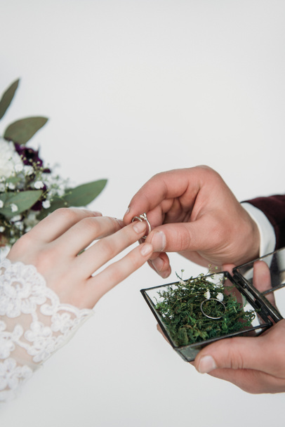 partial view of groom wearing wedding ring on bridal finger - Fotó, kép