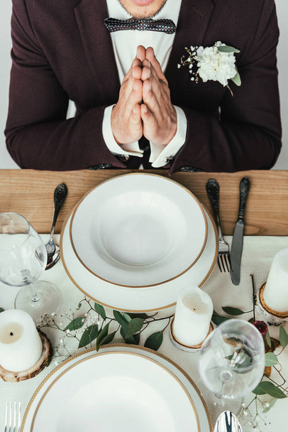 cropped shot of groom in suit praying while sitting at served table, rustic wedding concept - Photo, Image