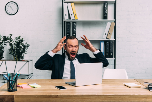 портрет перевантаженого бізнесмена в костюмі кричить на робочому місці з ноутбуком в офісі
 - Фото, зображення