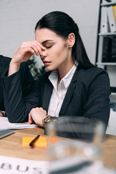 selective focus of tired businesswoman in suit at workplace in office - Fotoğraf, Görsel