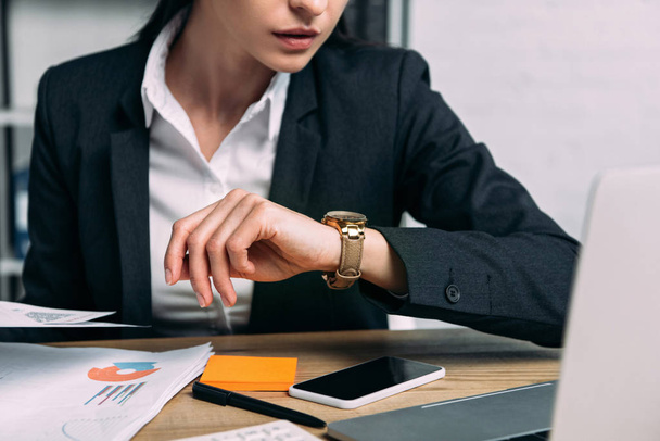 cropped shot of businesswoman in suit checking time at workplace in office - Фото, изображение