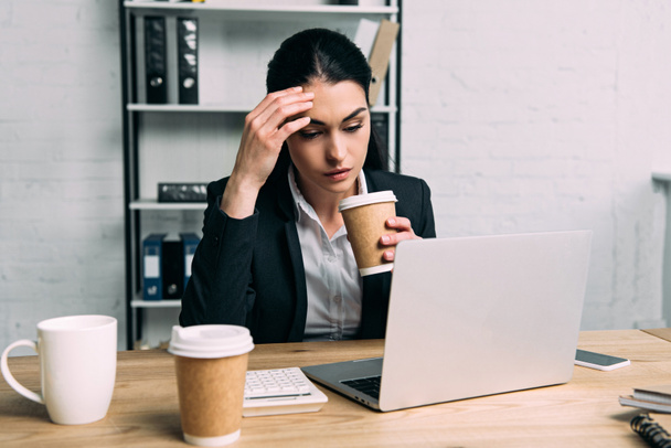 Müde Geschäftsfrau im Anzug mit Kaffee zum Arbeiten am Laptop am Arbeitsplatz im Büro - Foto, Bild