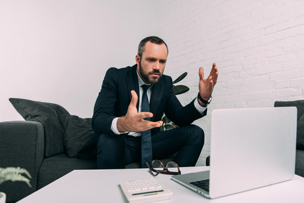 portrait of stressed businessman in suit looking at laptop on coffee table in office - Photo, Image