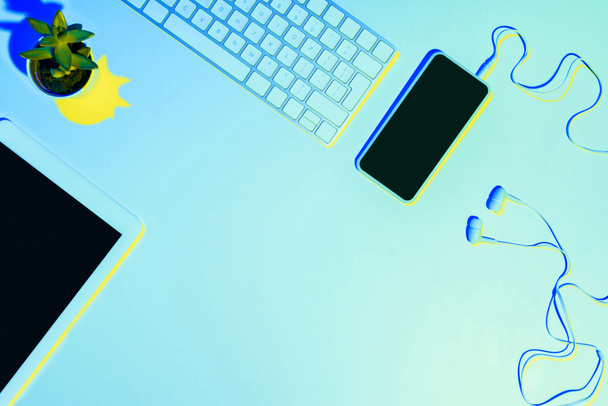 blue toned picture of smartphone, earphones, computer keyboard, plant and digital tablet  - Φωτογραφία, εικόνα