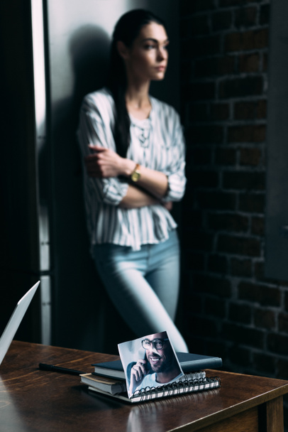 подавленная молодая женщина стоит одна и смотрит в сторону с фотографией бывшего парня на переднем плане
 - Фото, изображение