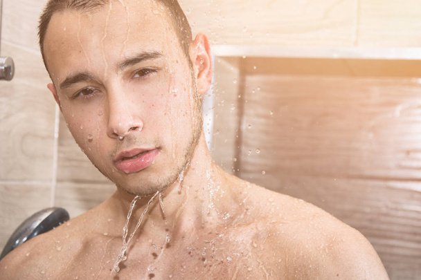 Young handsome guy in shower. Water, cleanliness and freshness. Sun, sea and vacation. Young sexy guy in shower. Handsome and attractive. Masculine and tanned - 写真・画像