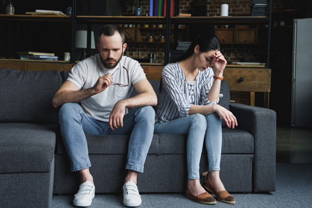 sad couple sitting on couch at home after quarrel and looking away - Photo, Image