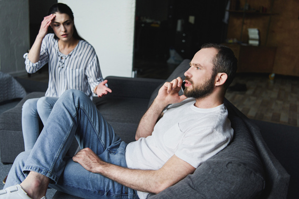 Hullu nainen puhuu miehelleen, kun hän puhuu puhelimitse sohvalla
 - Valokuva, kuva