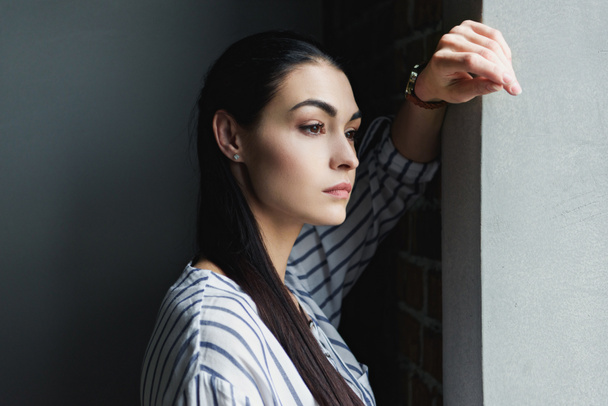 Zijaanzicht van depressieve jonge vrouw leunend op de muur en weg op zoek - Foto, afbeelding