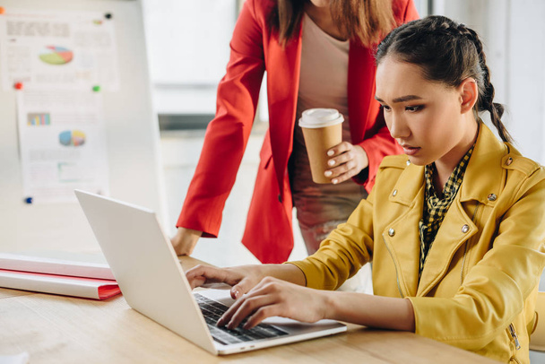 Geschäftsfrau hält Kaffeetasse in der Hand ihres Kollegen tippt auf Laptop in hellem Arbeitsraum - Foto, Bild