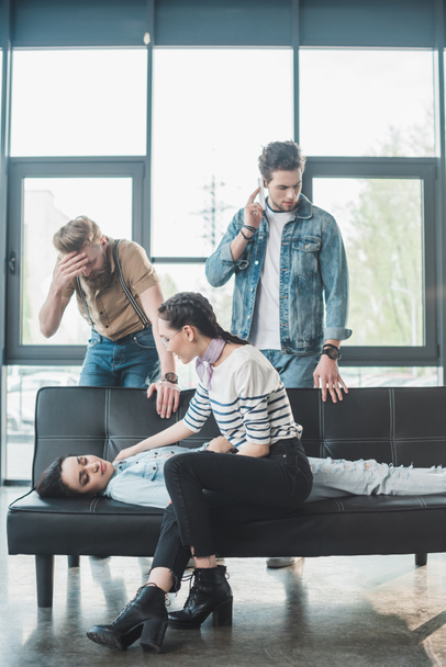 Men and woman worried about young fainted woman lying on sofa in office - Foto, imagen