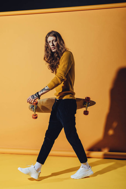 stylish tattooed skateboarder with longboard, on yellow - Photo, image