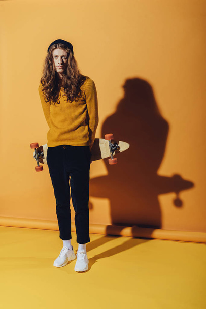 stylish young man posing with longboard, on yellow - Foto, afbeelding