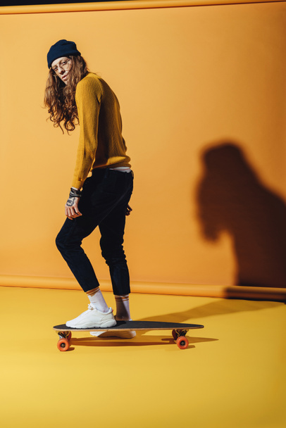 handsome stylish man standing on skateboard, on yellow - Fotoğraf, Görsel