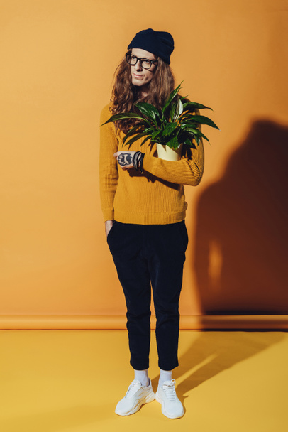 handsome fashionable man posing with green plant, on yellow - Fotó, kép