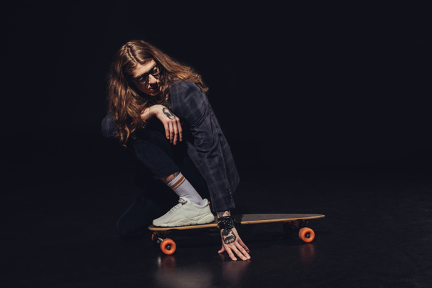 stylish man with long hair posing with longboard, on black - Photo, Image