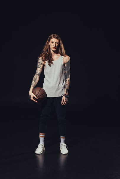 tattooed man standing with basketball ball, on black - Фото, зображення