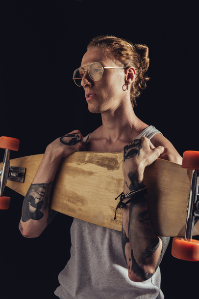 elegante tatuado homem segurando longboard, isolado no preto
 - Foto, Imagem