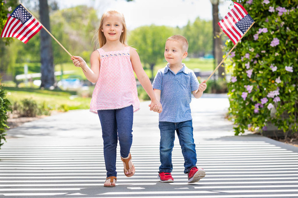 Молодая сестра и брат машут американскими флагами в парке
 - Фото, изображение