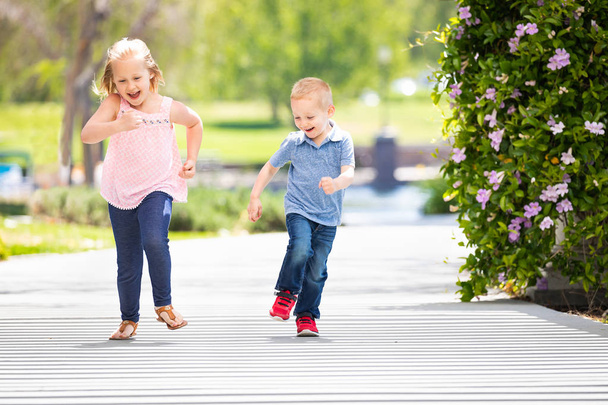 Молодые сестра и брат весело бегают в парке
 - Фото, изображение
