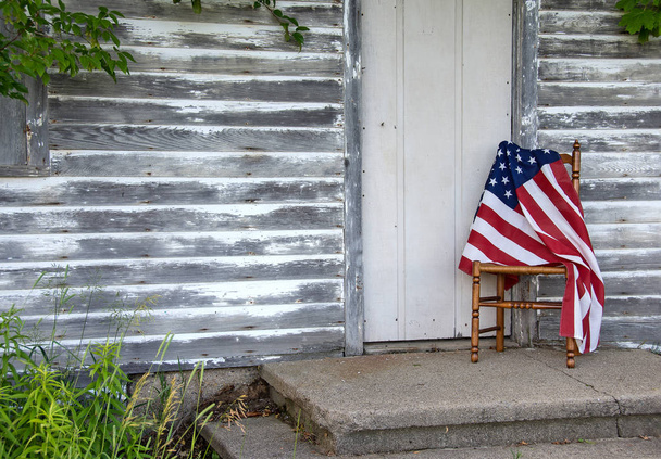American flag draped over old wooden chair by rustic house door - Foto, Imagem