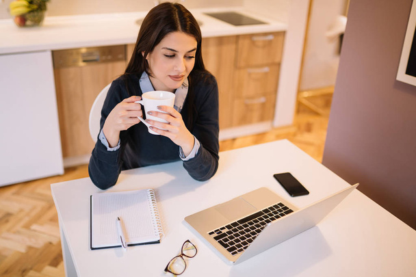 Młoda kobieta pijąc kawę siedząc przed laptop - Zdjęcie, obraz