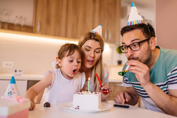 Jeune fille soufflant des bougies sur le gâteau d'anniversaire pendant qu'elle fête son anniversaire en famille
 - Photo, image