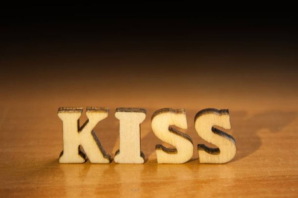 The word 'kiss' made of wooden letters. wood inscription on table and dark black background - Фото, зображення