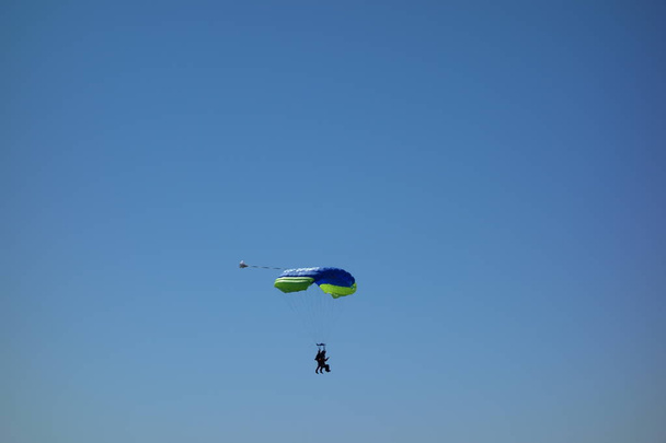 Парашютисты в тандеме. Пара парашютистов спускается на посадку. Ясное голубое небо
. - Фото, изображение