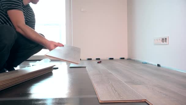 Young worker laying a floor with laminated flooring boards against window light - Footage, Video