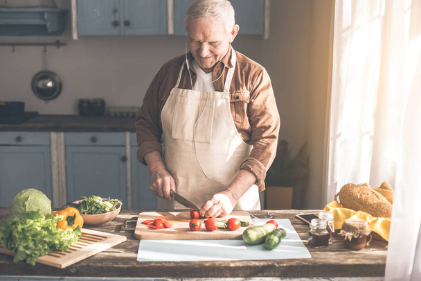 Joyful senior pensioner cutting vegetables in kitchen - 写真・画像