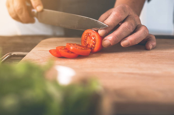 Old woman hands cutting tomato on wooden board - Foto, Bild