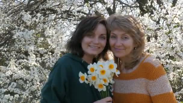 Matka i córka dorosły uśmiech siebie na wiosnę przed kwitnących drzew. Córka całuje mama w dzień matki - Materiał filmowy, wideo