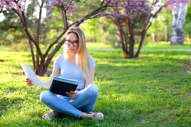 duro lavoro studentessa seduta su erba verde con cartella nera annuncio lettura
. - Foto, immagini