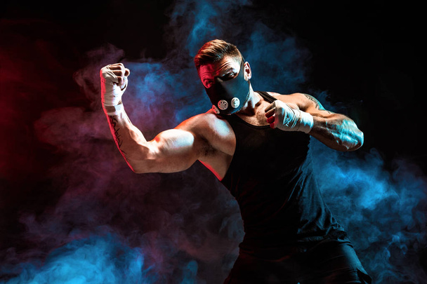 Strong male athlete in a black training mask on a black background - Valokuva, kuva