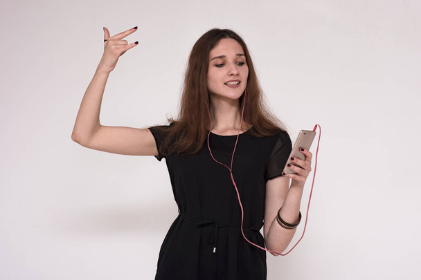 Portrait of a beautiful brunette girl on a gray background listening to music in headphones with a smartphone - Fotoğraf, Görsel