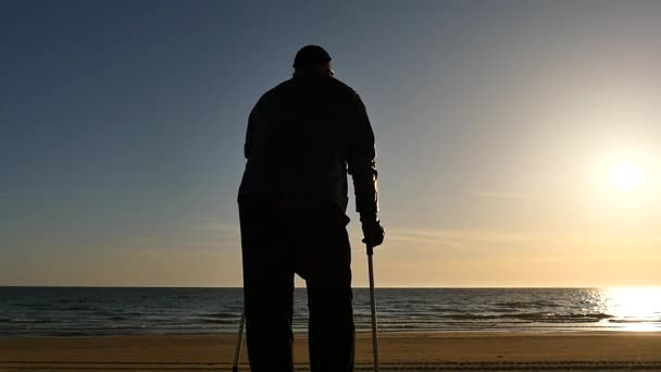 Niepełnosprawny mężczyzna sylwetka z kulami na plaży panoramy - Materiał filmowy, wideo
