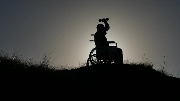 disabled man in wheelchair making gym excercise silhouette slow motion approaching camera - Footage, Video