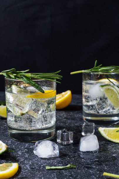 Alcoholic drink gin tonic cocktail with lemon, rosemary and ice on stone table - Photo, Image