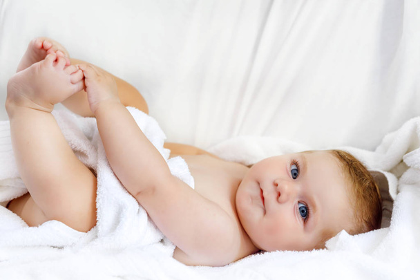 Lindo bebé jugando con sus propios pies después de tomar el baño. Adorable hermosa chica envuelta en toallas blancas
 - Foto, Imagen