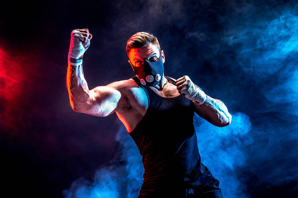 Strong male athlete in a black training mask on a black background - Fotografie, Obrázek