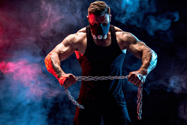 Portrait of muscular sportsman tearing metal chain. Black background with smoke - Photo, Image