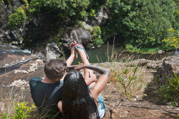 La joven pareja se sienta al borde de la ruptura en las cataratas y tomar un
  - Foto, Imagen