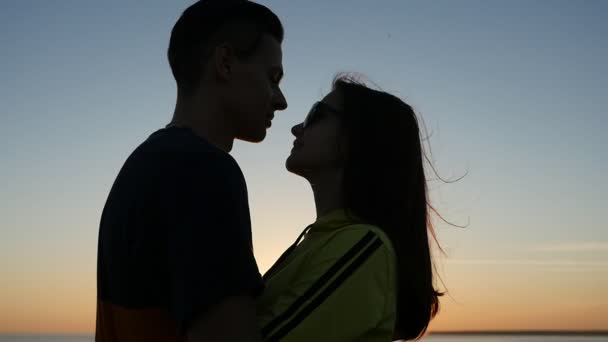 Romantikus lány, és ő vidám fiú van a Fekete-tenger partján napnyugtakor a nyári profil egy szerelmes pár, ölelni egymást, mosolyogva, és élvezi az élet: egy gyönyörű naplemente a Fekete-tenger partján a nyáron.  - Felvétel, videó