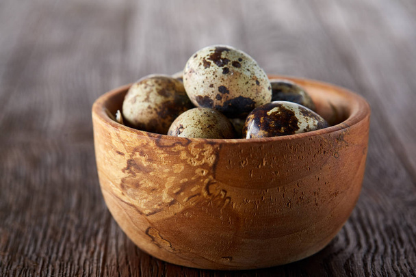 Fresh quail eggs in a wooden bowl on a dark wooden background, top view, close-up - Фото, зображення